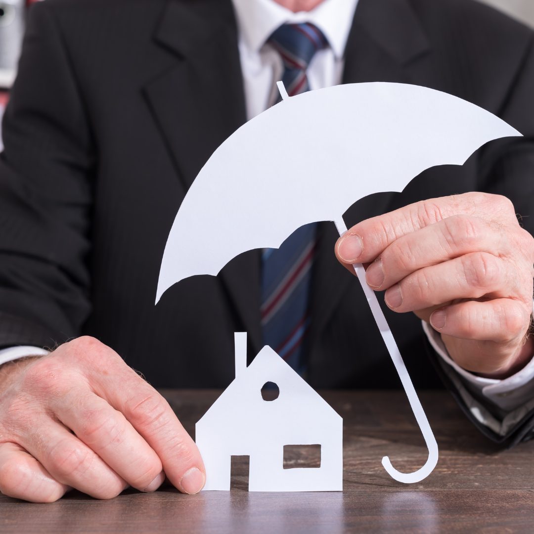 Ein Mann hält einen Miniregenschirm über ein Haus um es zu schützen